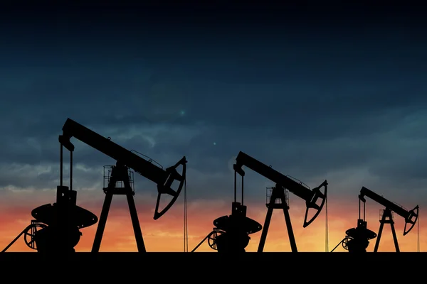 Silhouette of three oil pumps at sunset.