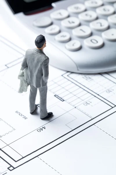 Businessman miniature with calculator on architect blueprint for housing cost