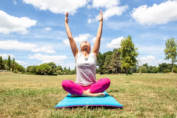 Meditating young woman doing yoga with stretched arms and upper body on exercise mat over summer blue sky