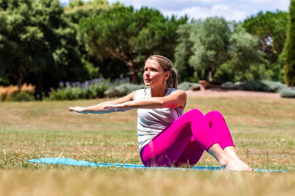 Sporty young blond woman toning up her arms and slimming her waist down on summer grass