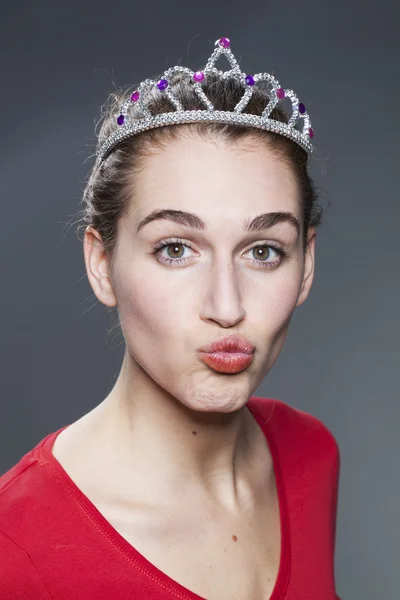 Cheeky 20s girl posing with a tiara on her head and making a pout for love