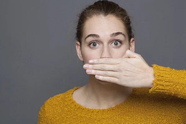 Stunned young woman covering her mouth for silence