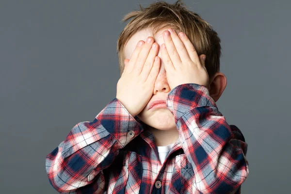 Unhappy young child covering his eyes with hands for sadness