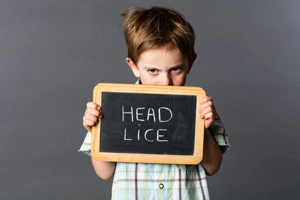 Ashamed preschool boy protecting from head lice behind school slate