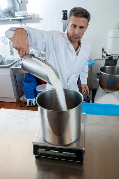 Professional cook pouring sugar to weight it on industrial scale