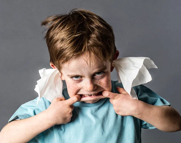 Silly kid with tissue in ears making grimace, not listening