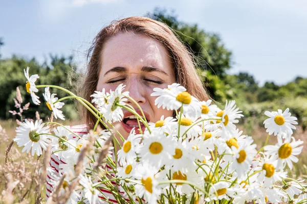 Young woman with pollen sickness sneezing, smelling a daisy bouquet