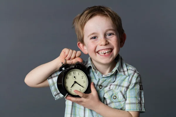 Joyful little boy with missing tooth showing an alarm clock