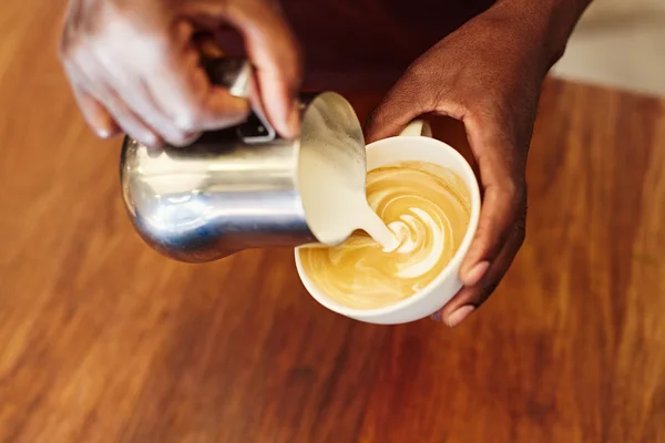 Barista pouring foamed milk in cup