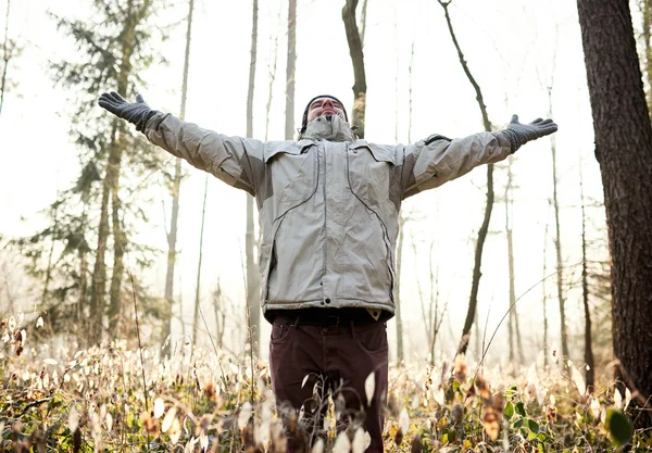 Man standing in forest lifting arms up