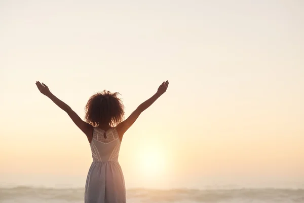 Woman standing on beach with arms raised