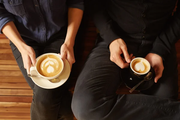 Couple sitting on bench and holding coffee
