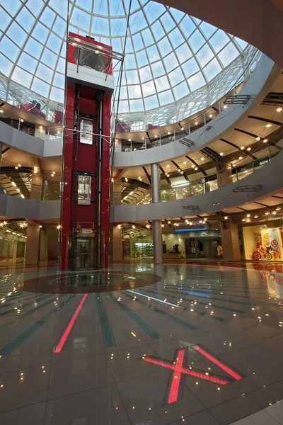 Huge hall of modern shopping centre with the glass lift, hours on a floor and a transparent glass dome