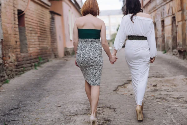 Two beautiful women walking on the street holding hands talking,
