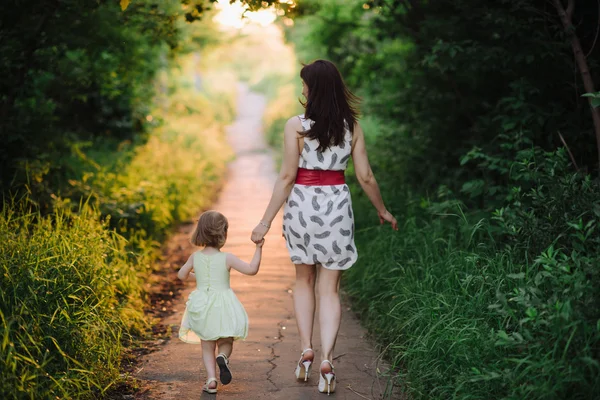 Mom keeps daughter's hand and walks the walk on the nature in sunset light