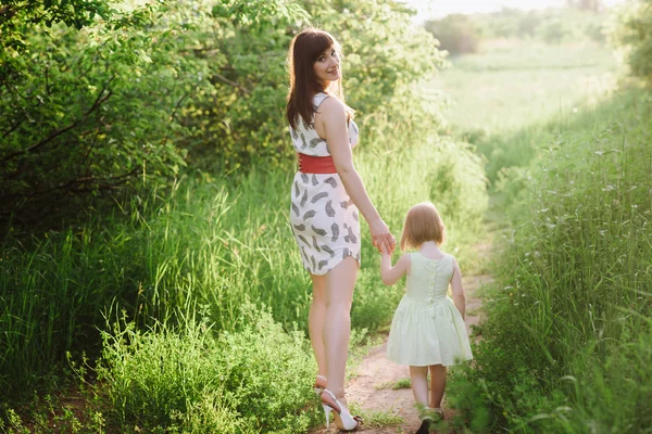 Mom keeps daughter\'s hand and walks the walk on the nature in sunset light