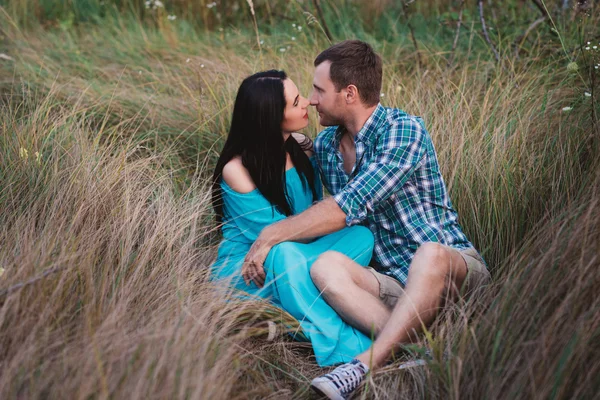 Shot of young man and woman sitting together outdoors on grass field.