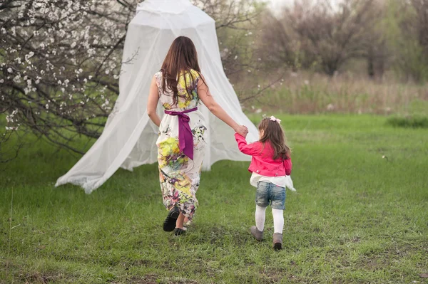 Mom plays with her daughter in the lush spring garden