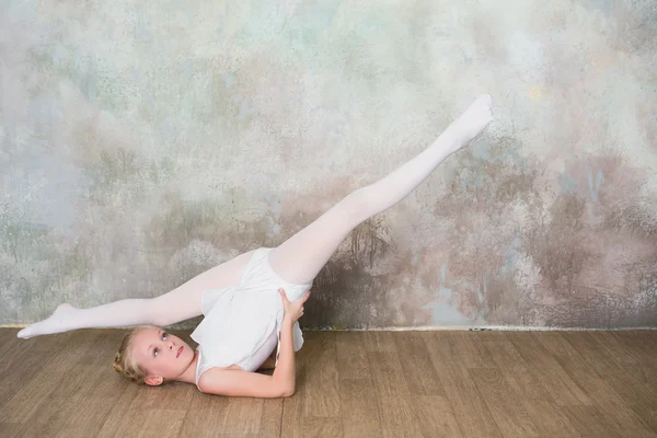 Little ballet dancer doing stretching before class in a white bathing suit
