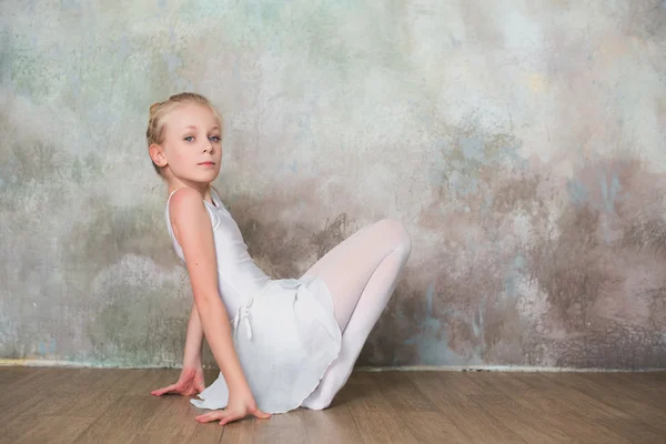 Little ballet dancer doing stretching before class in a white bathing suit