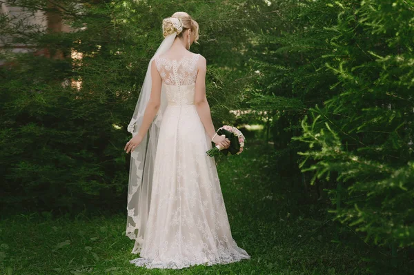 Stylish beautiful bride standing back in her wedding dress on nature