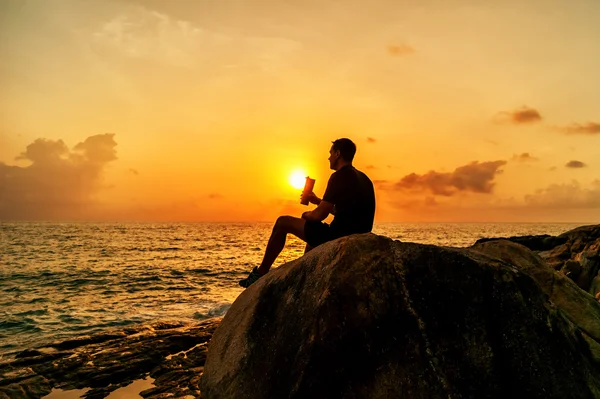 Man sitting on the rocks by the sea and watching the sunrise
