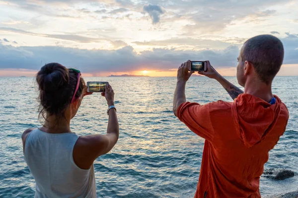 Young couple taking pictures on the beach at sunset background