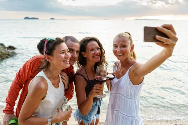 Young friends taking pictures on the beach at sunset background