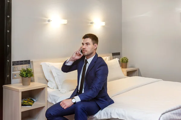 Young businessman calling on the phone sitting  the bed in the hotel