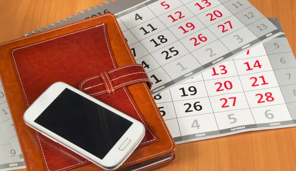 Brown personal organizer or planner with a mobile phone and a calendar on the desktop
