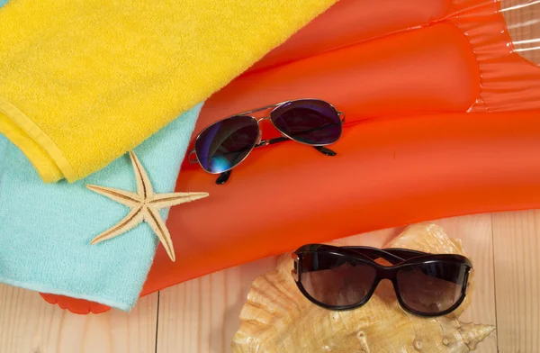 Summer beach accessories on swimming mattress. Sunglasses, towel, seashells