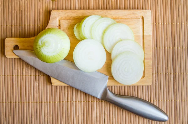 Onions, sliced on wooden cutting Board with a knife
