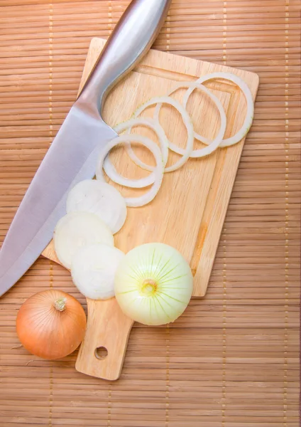 Onions, sliced on wooden cutting Board with a knife