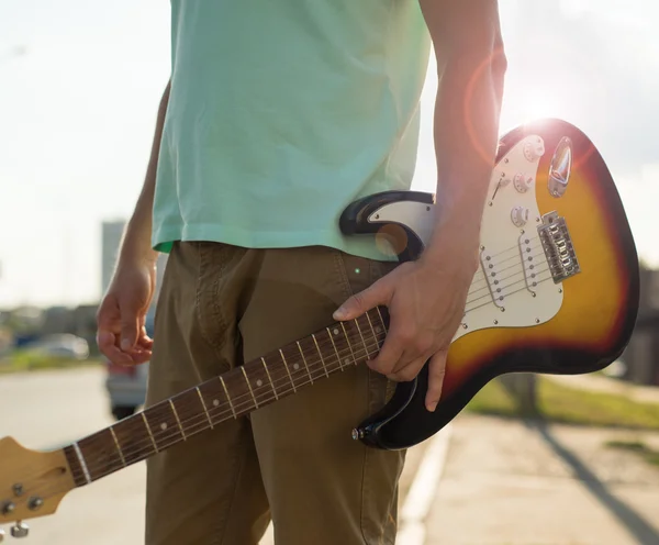 Young man hipster with a guitar stands on the road in the sunlight