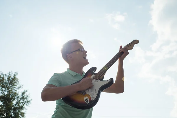 Young man with guitar singing in the sky and sunlight