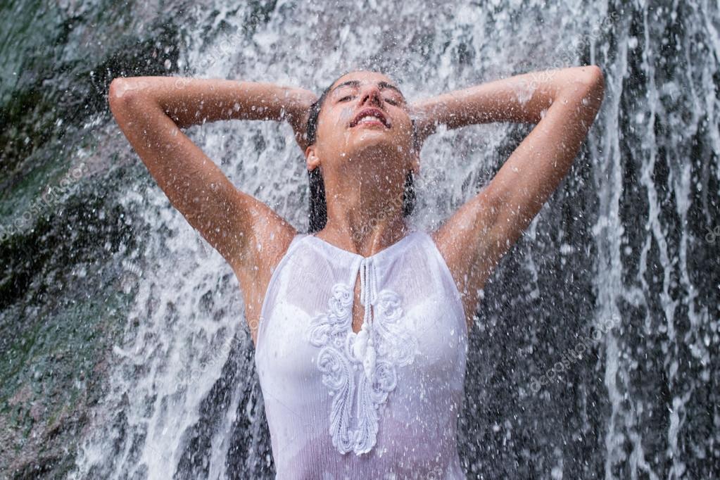 Очень красивая девушка с мокрыми волосами стоит под струями воды