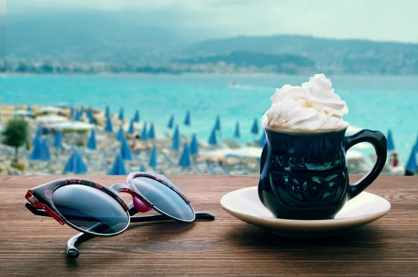 Summer Still Life. Coffee with cream and sunglasses on the background of the beach of the French Riviera. Enjoyable holiday concept