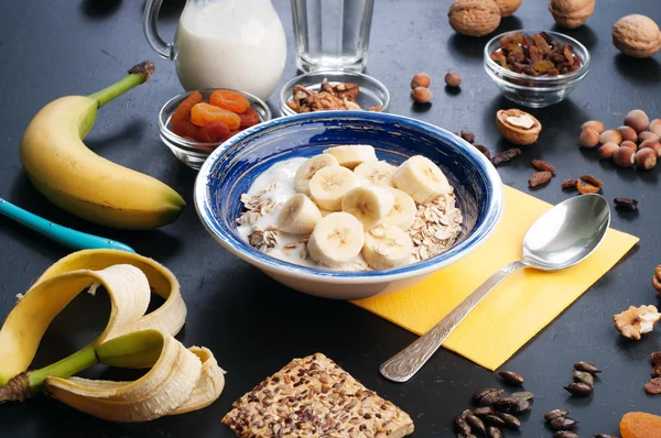 Useful and tasty breakfast with oatmeal, fruits, dried fruits and nuts on a dark surface. Healthy food concept. Useful vegetarian food