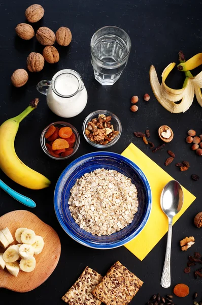 Useful and tasty breakfast with oatmeal, fruits, dried fruits and nuts on a dark surface. Healthy food concept. Useful vegetarian food