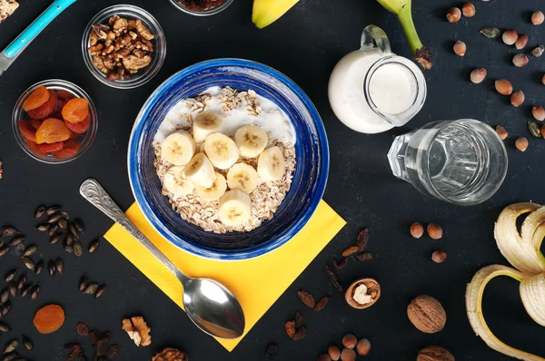 Useful and tasty breakfast with oatmeal, fruits, dried fruits and nuts on a dark surface. Healthy food concept. Useful vegetarian food