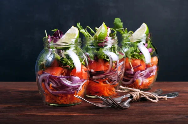 Salad with arugula, carrots, tomatoes, purple onion and lime in a glass jar. The concept of wholesome food home cooking, which you can take with you to work in a glass jar. Vegetarian salad. Useful dietary meal.