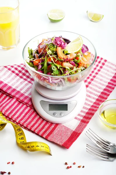Concept diet food. Light salad of arugula, tomato, purple onion and lime, which stands on the kitchen scales.. Next measuring tape symbolizing measurement of body volume during a diet. Vegetarian low-fat food.