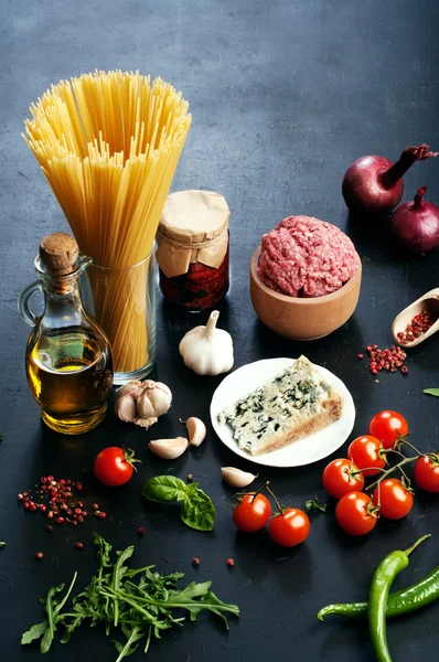 Italian food concept. Ingredients for cooking pasta, such as pasta, onions, tomatoes, olive oil, ground beef, basil leaves and cheese on dark board. Place for writing text