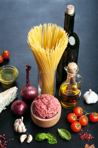 Italian food concept. Ingredients for cooking pasta, such as pasta, onions, tomatoes, olive oil, ground beef, cheese, and basil leaves on a black board