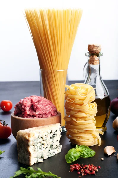 Italian food concept. Ingredients for cooking pasta, such as pasta, onions, tomatoes, olive oil, ground beef, cheese, and basil leaves on a black board. White background. Place for writing text