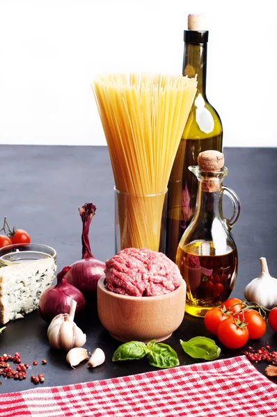 Italian food concept. Ingredients for cooking pasta, such as pasta, onions, tomatoes, olive oil, ground beef, cheese, and basil leaves on a black board. White background. Place for writing text
