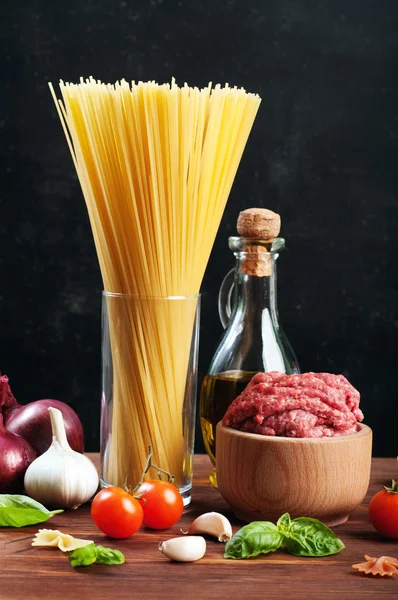 Italian food concept. Ingredients for cooking pasta, such as pasta, olive oil, ground beef and basil leaves on a brown wooden board. Black background. Place for writing text