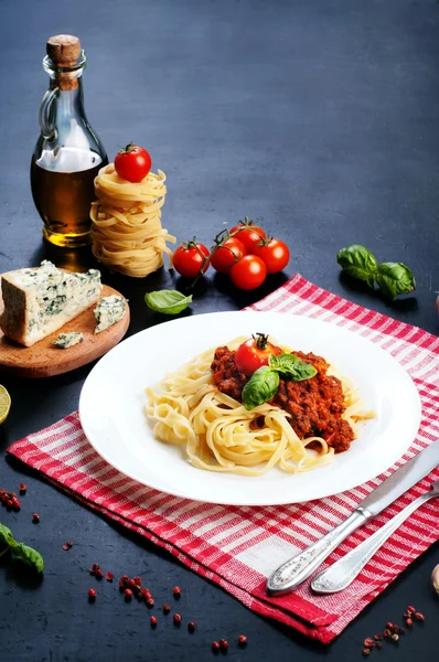 Pasta bolognese in white plate on a white and a red napkin. Beside the ingredients for making pasta. Italian Cuisine