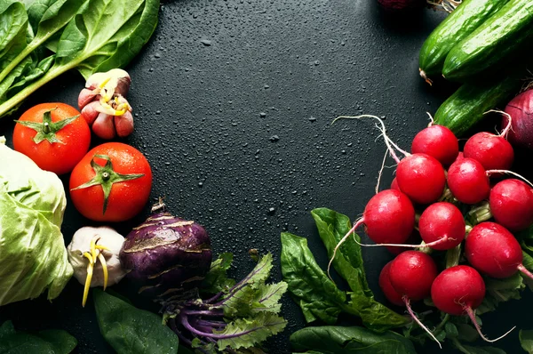 Fresh juicy vegetables and greenery, such as onions, tomatoes, spinach, hot pepper, garlic, cabbage, kohlrabi, and radishes on a black surface. Vegetable background. Vegan concept. Space for text