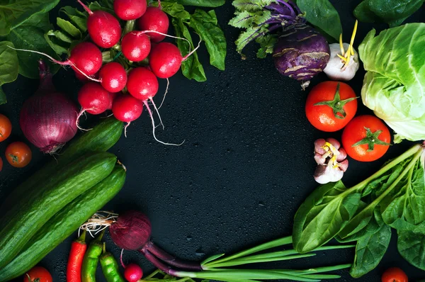 Fresh juicy vegetables and greenery, such as onions, tomatoes, spinach, hot pepper, garlic, cabbage, kohlrabi, and radishes on a black surface. Vegetable background. Vegan concept. Space for text